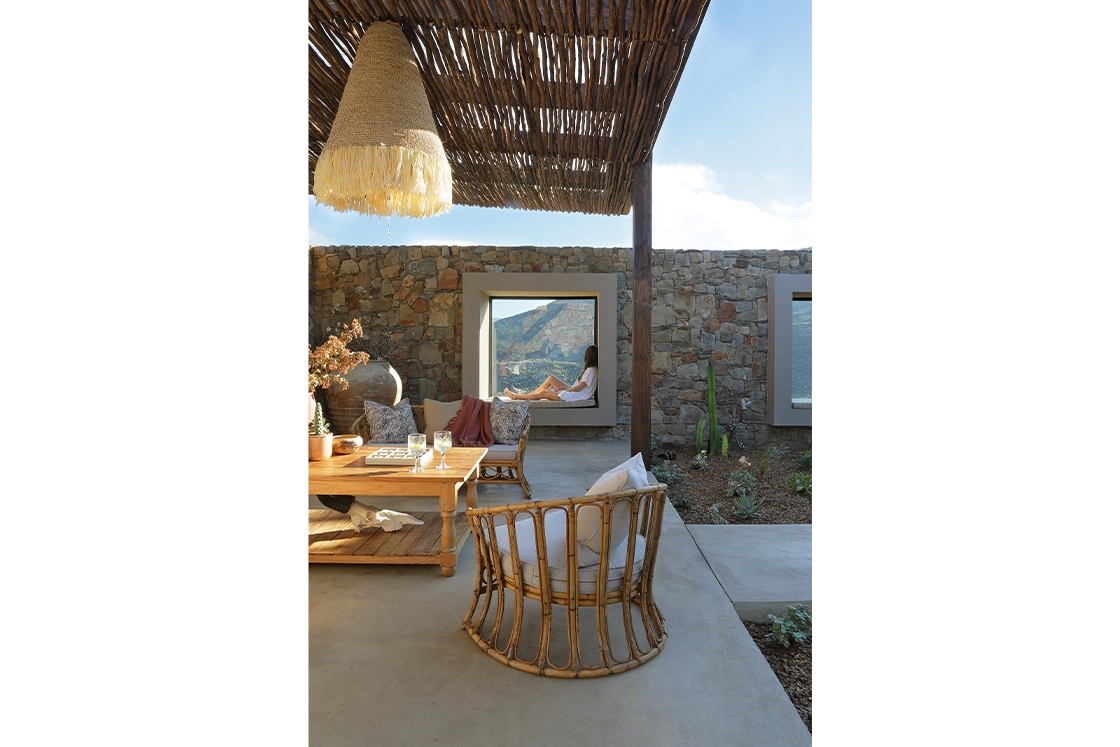 Perfect Hideaways real estate property: Outdoor seating area with rustic decor, stone walls, and a large window framing a mountain view. A person relaxes on the window ledge. Wolwehoek Private Nature Reserve, Montagu.