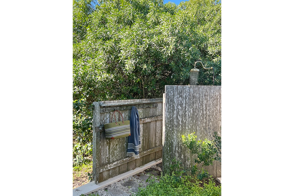 Perfect Hideaways property for sale: An outdoor shower surrounded by greenery, with a rustic wooden fence and hooks holding towels and a bag, exuding a natural and refreshing vibe. Yellowwood Cottage, Churchhaven.