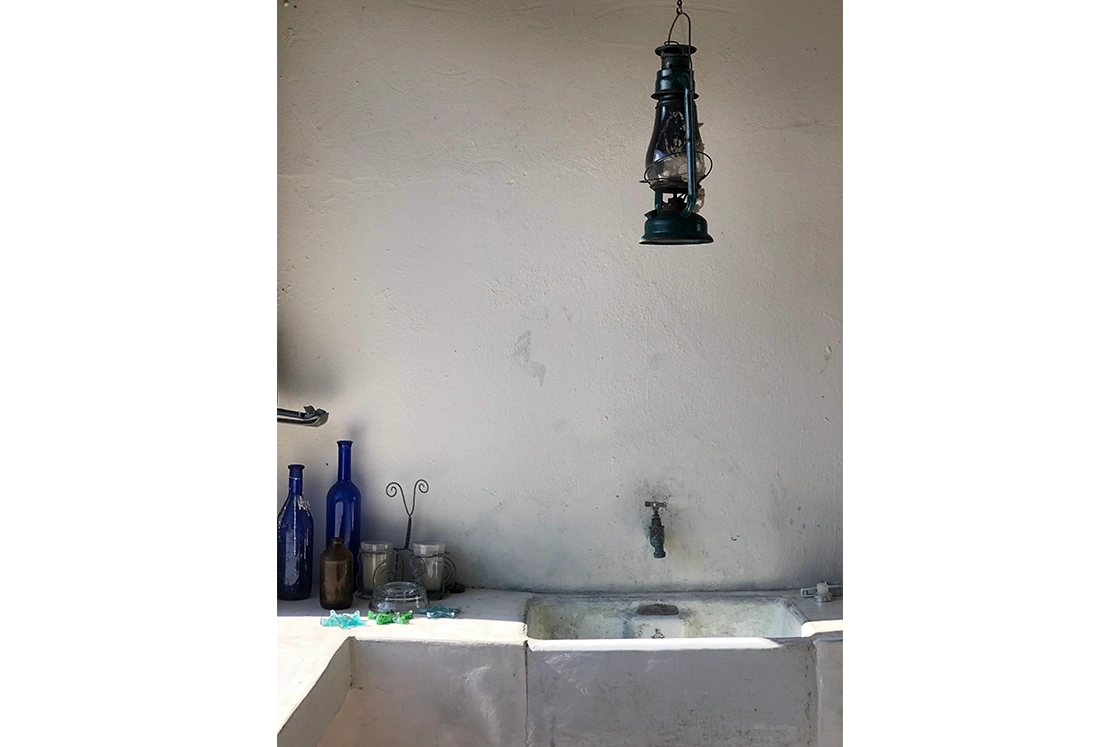 Perfect Hideaways property for sale: Rustic sink with old faucet against a plain wall. Blue glass bottles and jars sit on the counter. A vintage lantern hangs above, creating a nostalgic vibe. The Cottage in Churchhaven.