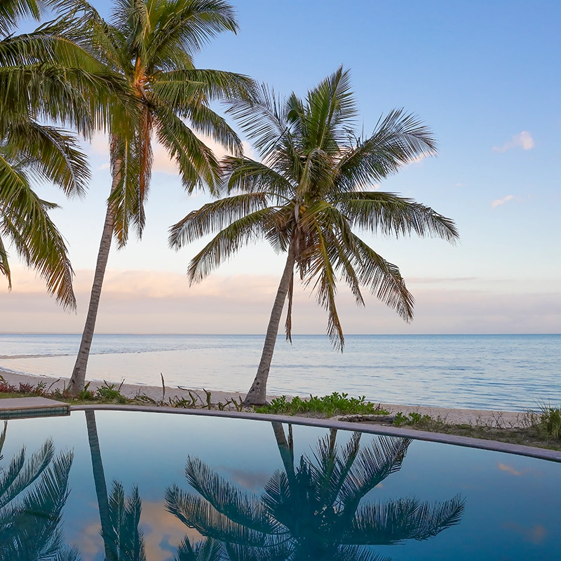 Perfect Hideaways real estate property: Large beachside pool with beach access, showcasing nearby palm trees and local fishing vessels. Villa Tanga, Benguerra Island.