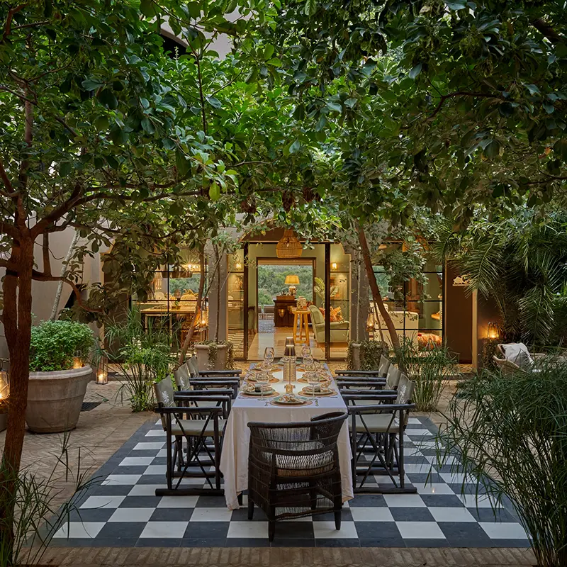 Perfect Hideaways property for sale: Cozy outdoor dining area with a long table set for dinner, surrounded by lush green trees and plants. Warm lighting from lanterns creates an inviting atmosphere. Ukuthula House in Mpumalanga.