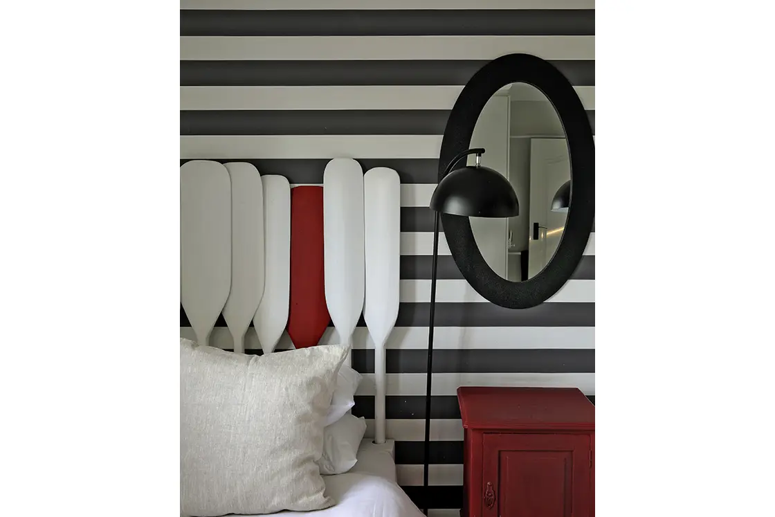 Perfect Hideaways real estate property: Bedroom with black and white striped walls features a headboard made of white and red paddles. A black oval mirror and red side table add contrast. Fynbos Cottage, Churchhaven.