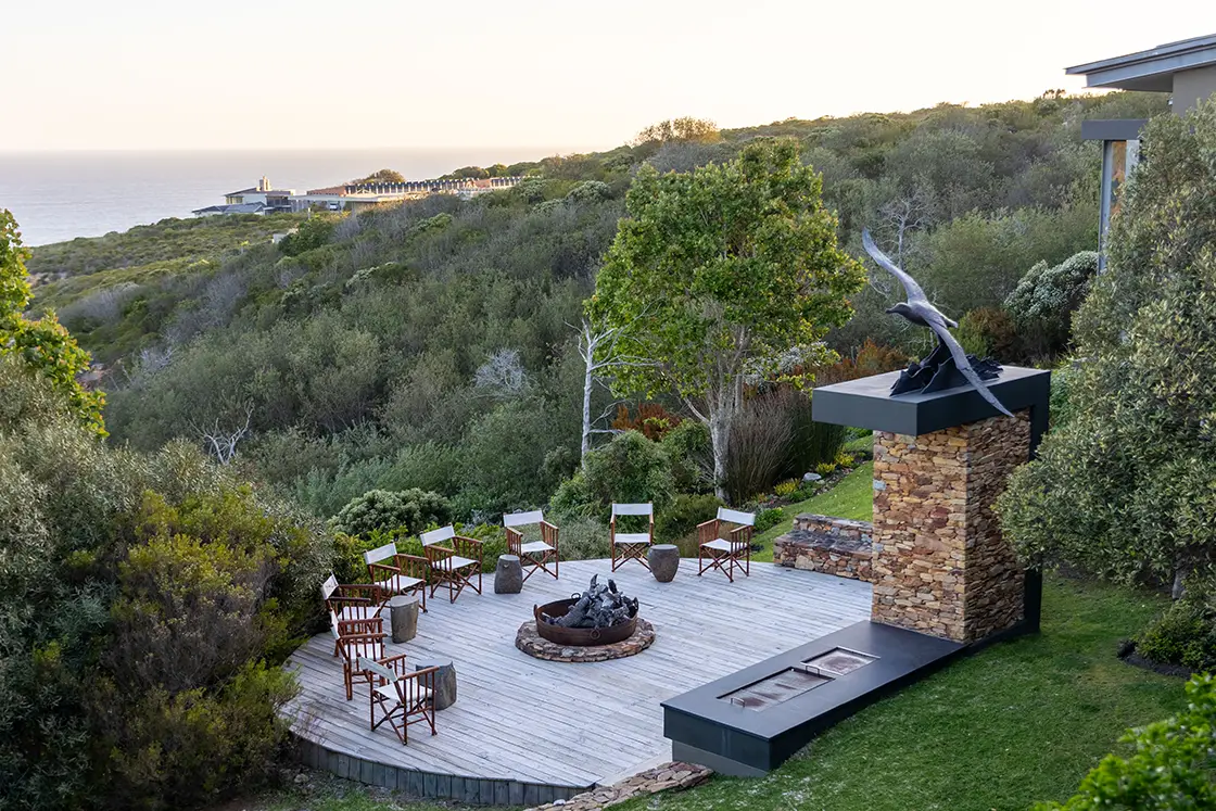 Perfect Hideaways real estate property: Scenic outdoor seating area on a wooden deck with chairs around a fire pit. Set in lush greenery with ocean view, conveying a serene and inviting atmosphere. Knysna, Ocean’s Edge.