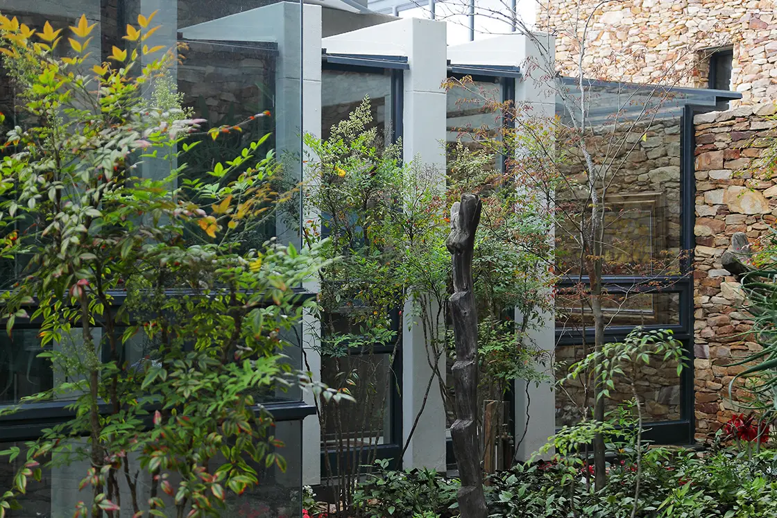 Perfect Hideaways real estate property: Modern building with large glass windows surrounded by lush greenery and a stone wall. The scene conveys a serene, natural atmosphere. Knysna, Ocean’s Edge.