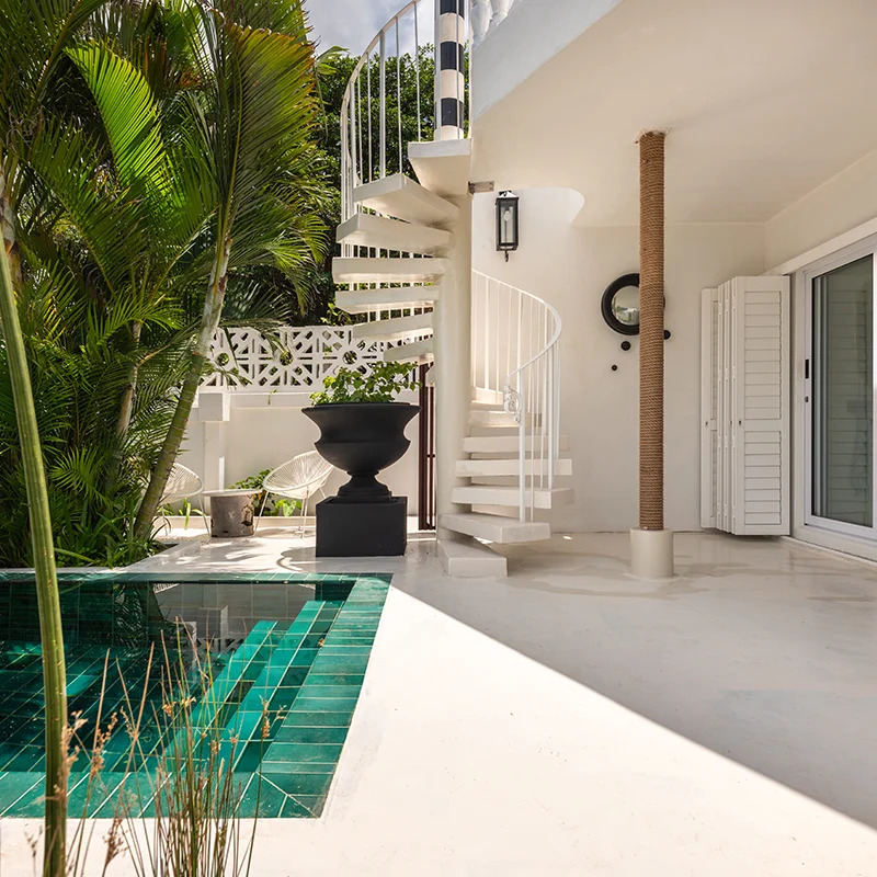 Perfect Hideaways real estate property: Modern terrace with a spiral staircase, green-tiled pool, and lush plants. Open sliding doors reveal a stylish interior. Bright, serene atmosphere. Five on Main, Ballito.