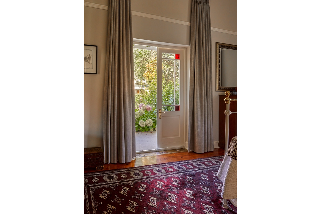 Perfect Hideaways real estate property: A bathroom featuring a freestanding bathtub next to a window with striped curtains; the second image shows a doorway with light-colored curtains revealing a garden outside. Montagu, Montagu Vines Guesthouse.