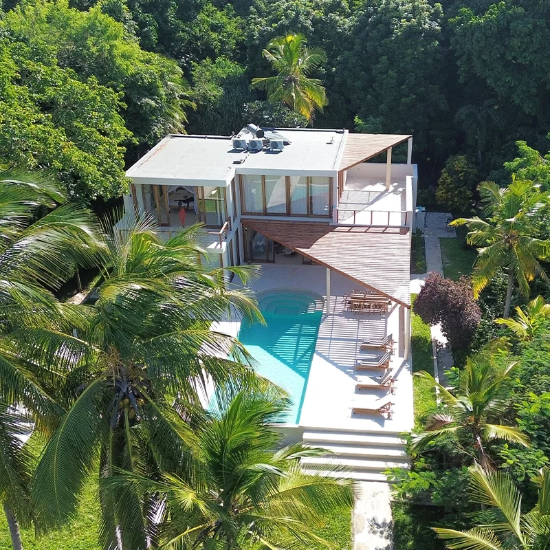 Perfect Hideaways real estate property: Modern tropical luxury villa with private swimming pool, surrounded by dense jungle and palm trees, aerial drone view, minimalist architecture with large glass windows, sun loungers on pool deck, secluded eco resort setting. Under the Stars Villa, Msambweni.