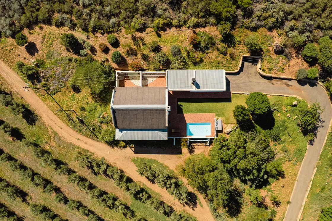 Perfect Hideaways real estate property: Aerial view of a modern house with a flat roof, surrounded by lush greenery and trees. A swimming pool is visible beside the house. The scene is peaceful. Cloeten Farm & Guest Cottages, Robertson.
