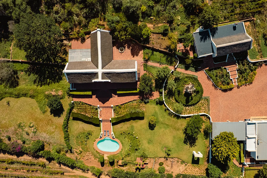Perfect Hideaways real estate property: Aerial view of an elegant estate with a cross-shaped roof, surrounded by lush greenery. A small pool and landscaped gardens enhance the tranquil setting. Cloeten Farm & Guest Cottages, Robertson.