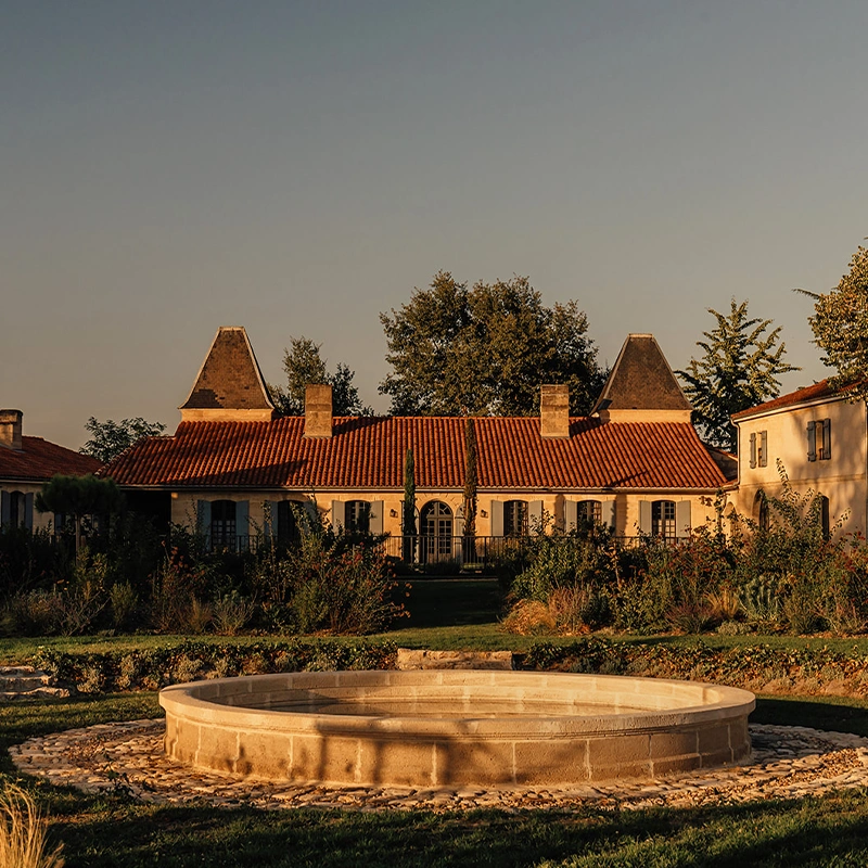 Perfect Hideaways real estate property: Traditional French country estate with terracotta roof tiles, manicured gardens, and a circular stone fountain, bathed in warm evening light. Château Beaulieu, Abzac.