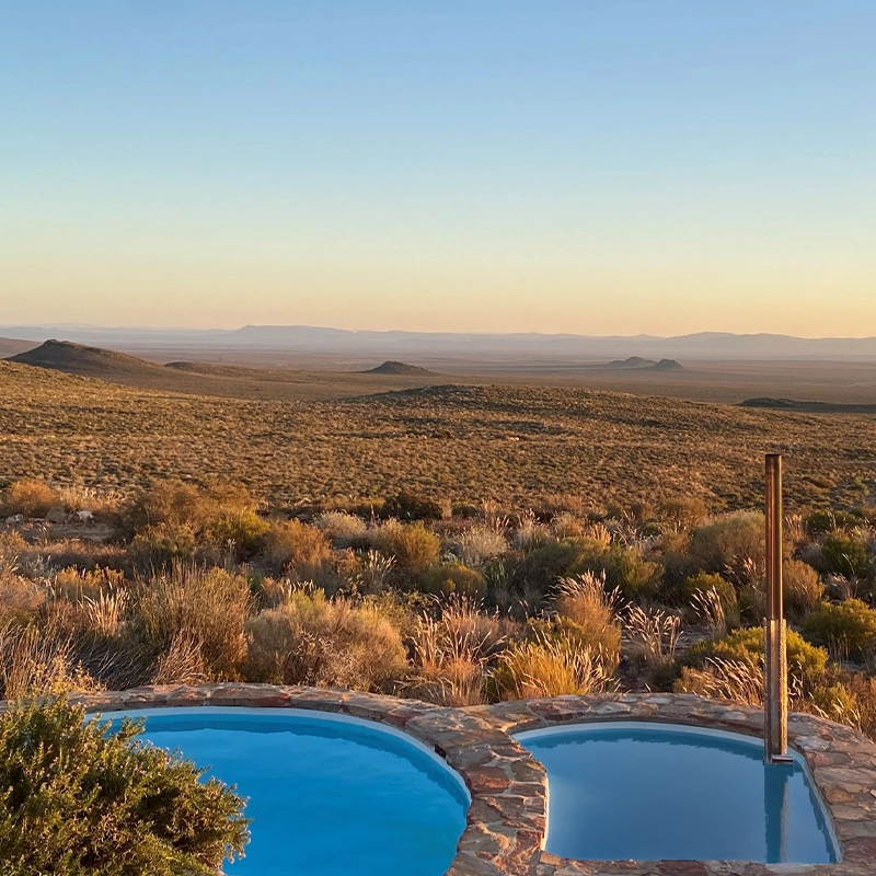 Perfect Hideaways real estate property: Private plunge pool overlooking a vast semi-arid wilderness and distant mountains at golden hour, surrounded by native scrub and rugged hills. Tierkloof Mountain Cottages, Karoo.